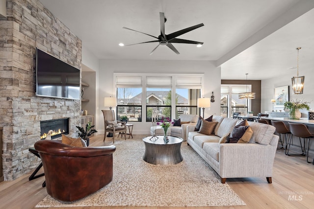 living room with a stone fireplace, recessed lighting, ceiling fan with notable chandelier, baseboards, and light wood-style floors