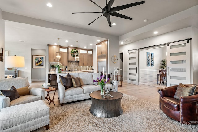 living area with a barn door, baseboards, ceiling fan, light wood-type flooring, and recessed lighting