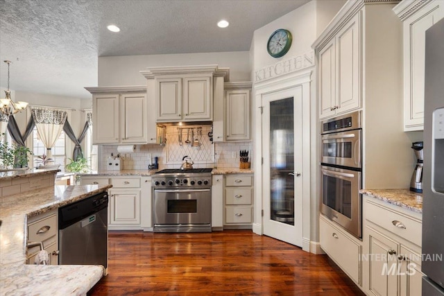 kitchen with appliances with stainless steel finishes, backsplash, dark hardwood / wood-style flooring, hanging light fixtures, and light stone counters