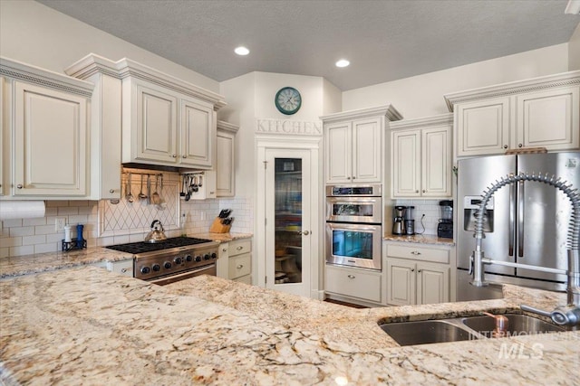 kitchen featuring sink, light stone counters, a textured ceiling, stainless steel appliances, and decorative backsplash