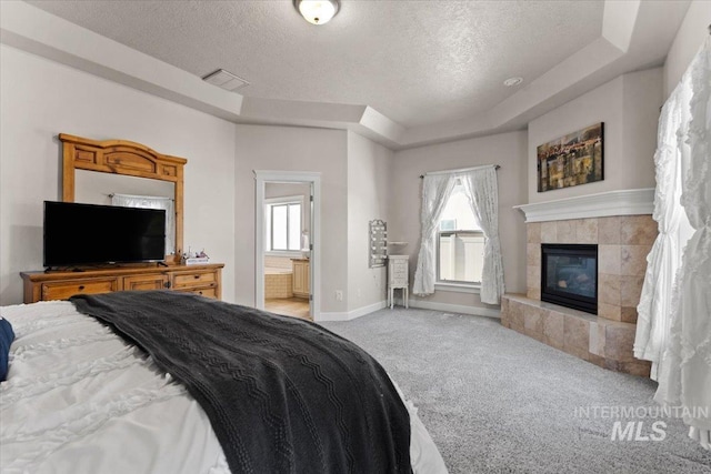 bedroom featuring a tray ceiling, a tile fireplace, a textured ceiling, and carpet flooring