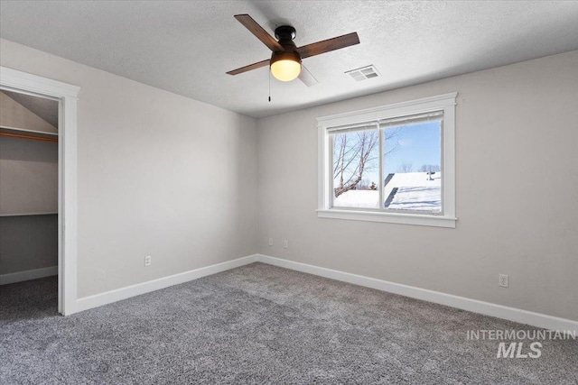 unfurnished bedroom featuring a spacious closet, a textured ceiling, carpet flooring, a closet, and ceiling fan