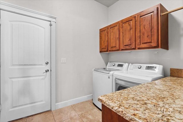 clothes washing area featuring cabinets, washing machine and dryer, and light tile patterned floors