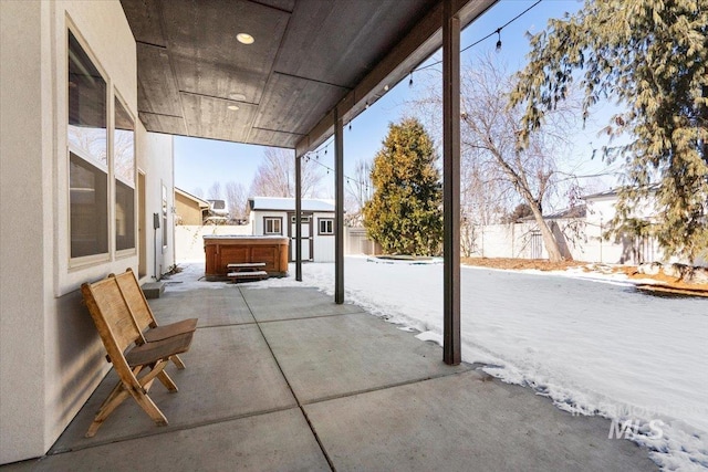 snow covered patio with an outdoor structure and a hot tub