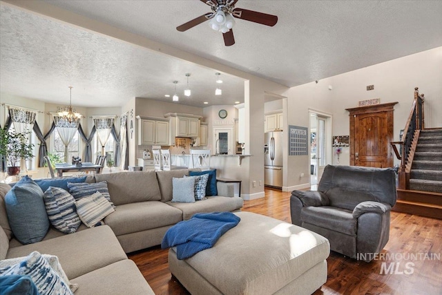 living room with ceiling fan with notable chandelier, light hardwood / wood-style floors, and a textured ceiling