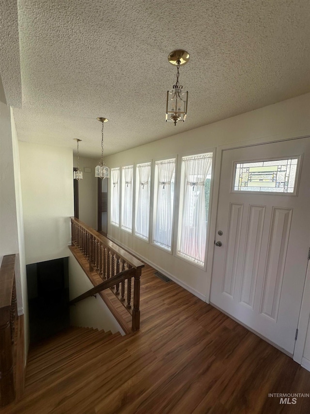 foyer entrance featuring a notable chandelier, a textured ceiling, and dark wood-type flooring