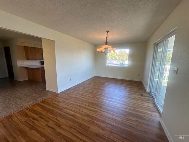 unfurnished dining area with dark wood-type flooring, a textured ceiling, and a chandelier