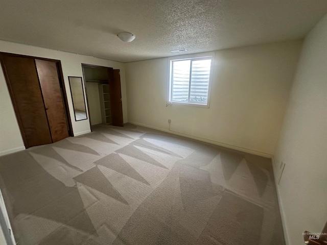 unfurnished bedroom with light carpet, a textured ceiling, and two closets