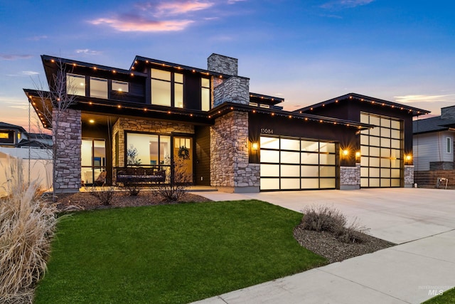 contemporary home featuring concrete driveway, a front yard, covered porch, a garage, and stone siding