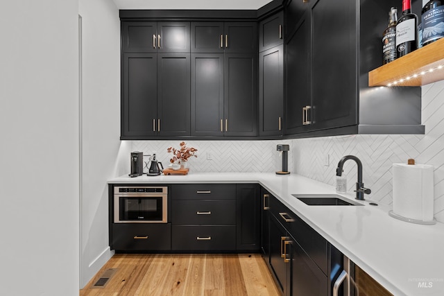 13684 N Sage Grouse Pl, Boise, ID 83714 - kitchen with a sink, backsplash, dark cabinetry, light wood finished floors, and light countertops