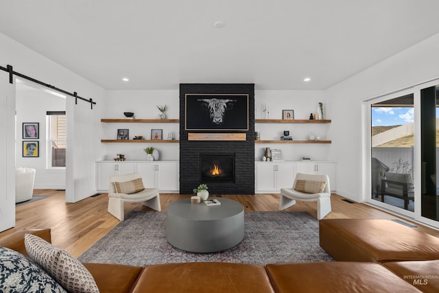 13684 N Sage Grouse Pl, Boise, ID 83714 - living room featuring baseboards, light wood finished floors, recessed lighting, a barn door, and a brick fireplace