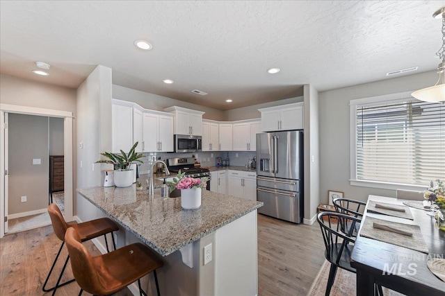 kitchen with appliances with stainless steel finishes, a sink, a peninsula, a breakfast bar, and white cabinetry