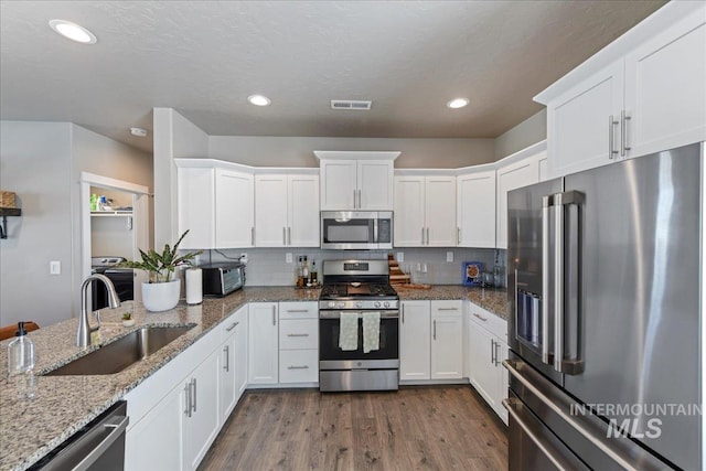 kitchen with visible vents, a sink, stainless steel appliances, white cabinetry, and dark wood-type flooring
