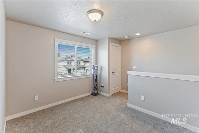 spare room with a textured ceiling, visible vents, baseboards, light carpet, and recessed lighting