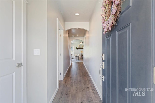 hallway featuring arched walkways, baseboards, recessed lighting, and wood finished floors
