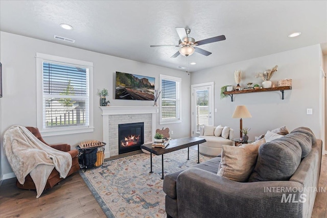 living area with ceiling fan, a brick fireplace, light wood-style flooring, baseboards, and visible vents