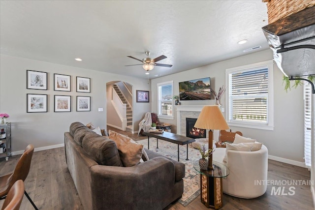 living area with visible vents, arched walkways, a ceiling fan, baseboards, and a lit fireplace