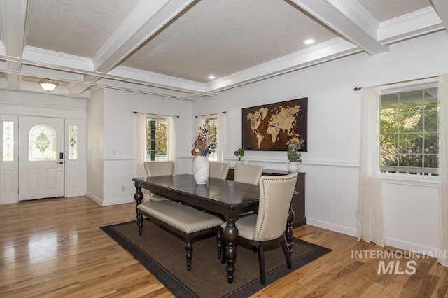 dining area with light wood-style floors, crown molding, and beam ceiling