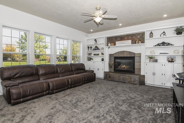 living area with built in features, ceiling fan, a textured ceiling, a fireplace, and dark carpet