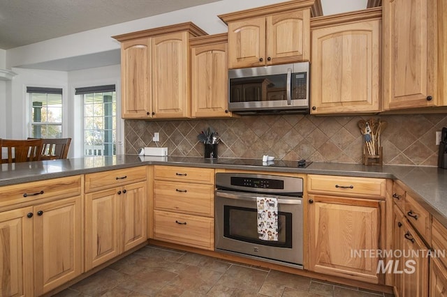 kitchen with stainless steel appliances, dark countertops, backsplash, light brown cabinetry, and stone finish flooring