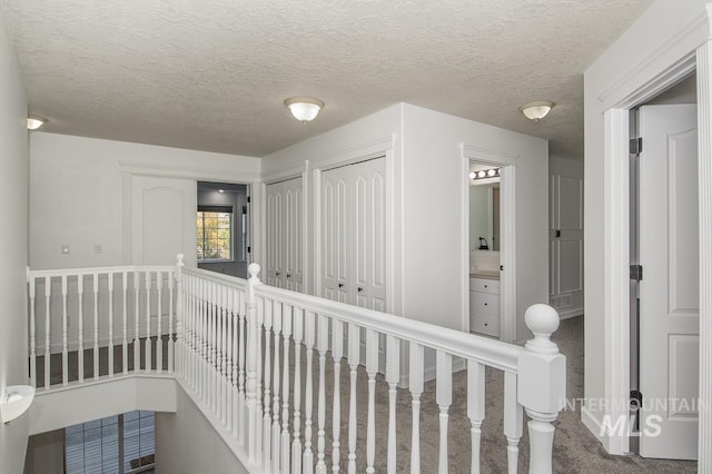 hallway featuring a textured ceiling, carpet flooring, and an upstairs landing