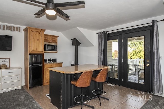 kitchen featuring visible vents, brown cabinetry, freestanding refrigerator, built in microwave, and a kitchen bar