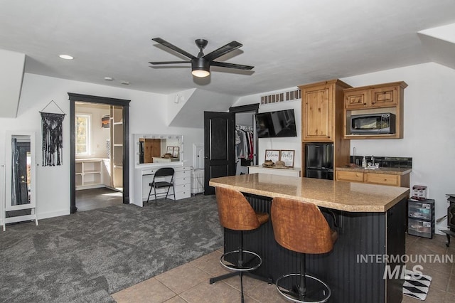 kitchen with a kitchen breakfast bar, light countertops, freestanding refrigerator, built in microwave, and dark colored carpet