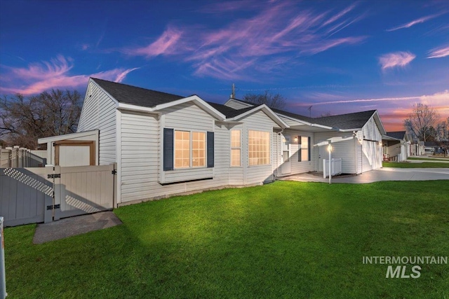 back house at dusk featuring a lawn and a garage