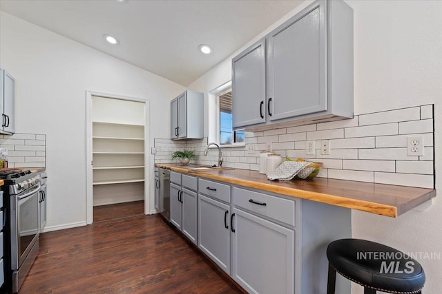 kitchen featuring sink, butcher block countertops, lofted ceiling, gray cabinets, and appliances with stainless steel finishes