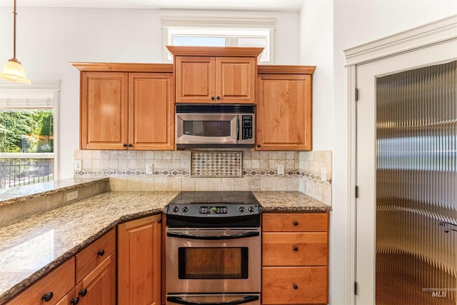 kitchen featuring backsplash, brown cabinetry, light stone countertops, hanging light fixtures, and appliances with stainless steel finishes