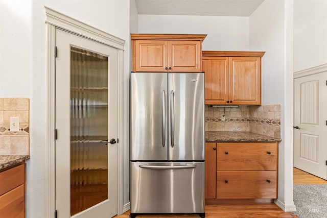 kitchen featuring dark stone counters, decorative backsplash, light wood-style floors, and freestanding refrigerator