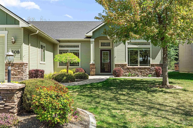 craftsman house with board and batten siding, stone siding, a front lawn, and a shingled roof