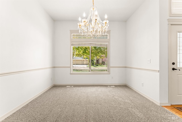 empty room featuring a chandelier, a wealth of natural light, carpet flooring, and baseboards