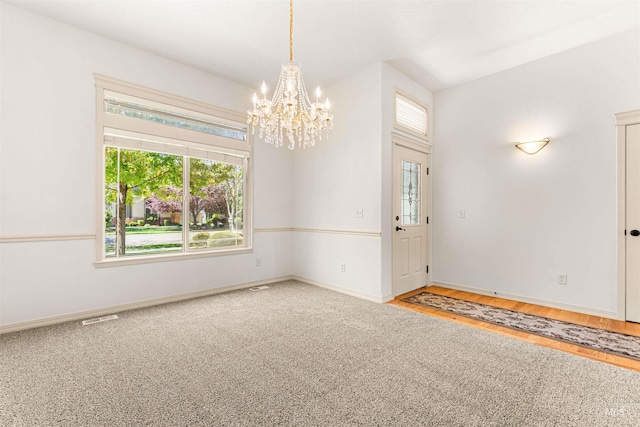 empty room with wood finished floors, baseboards, a chandelier, and a healthy amount of sunlight