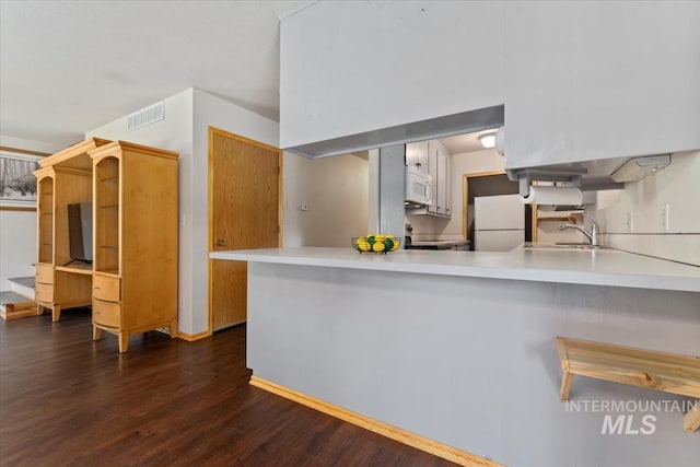 kitchen featuring white cabinets, sink, kitchen peninsula, white appliances, and dark hardwood / wood-style flooring