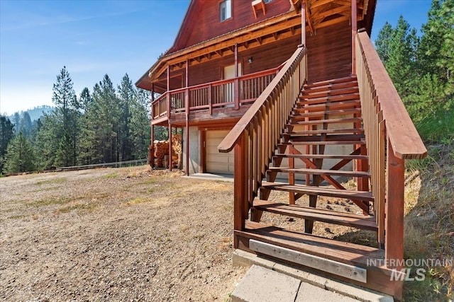 exterior space with an attached garage, dirt driveway, stairway, and a forest view