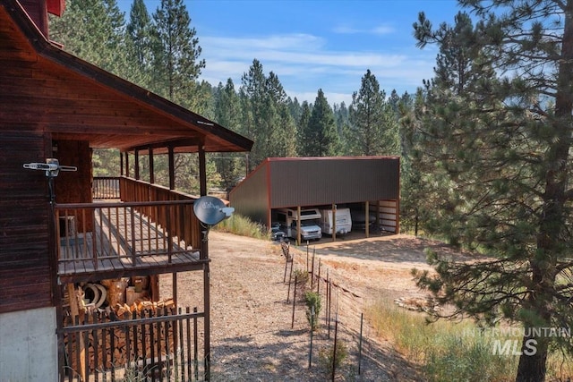 exterior space featuring dirt driveway, a wooded view, and a carport