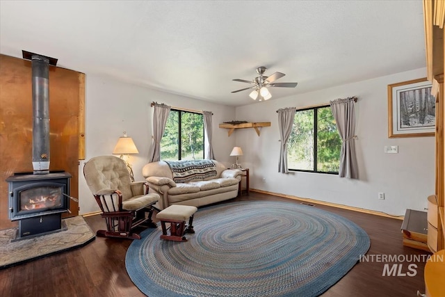 living room with baseboards, a ceiling fan, wood finished floors, and a wood stove