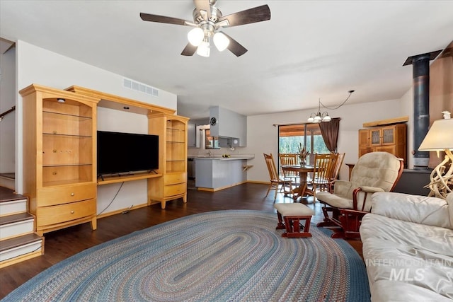 living room featuring visible vents, dark wood-type flooring, ceiling fan with notable chandelier, and a wood stove
