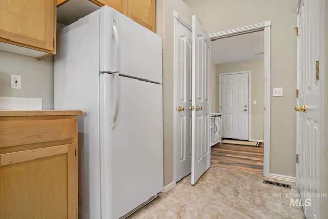 kitchen with freestanding refrigerator, light brown cabinetry, baseboards, and visible vents