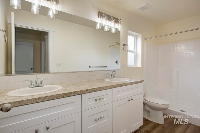 bathroom featuring toilet, backsplash, hardwood / wood-style floors, a shower, and vanity