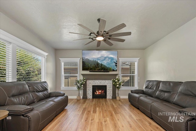 living room featuring ceiling fan, light wood finished floors, baseboards, and a tiled fireplace