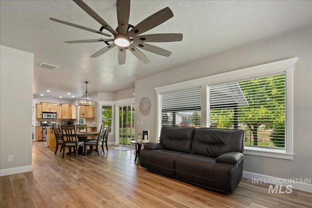 living area with baseboards, a ceiling fan, light wood-type flooring, a textured ceiling, and recessed lighting
