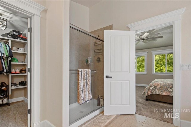 ensuite bathroom featuring a stall shower, ceiling fan, tile patterned floors, and a walk in closet