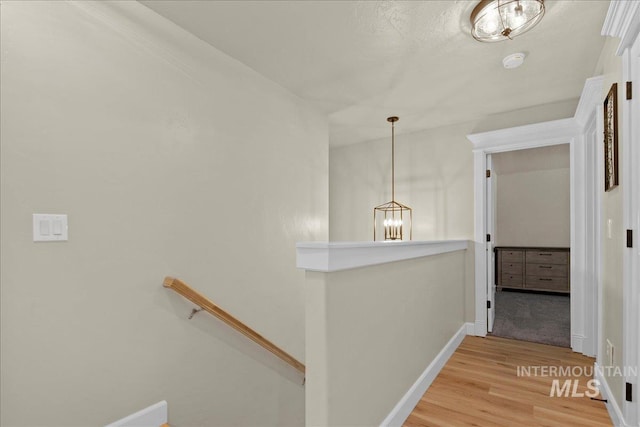 hall featuring an upstairs landing, light wood-style flooring, baseboards, and a chandelier