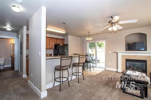 kitchen with dark carpet, black fridge, a tile fireplace, and a breakfast bar area