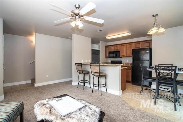 kitchen featuring ceiling fan with notable chandelier, light colored carpet, a breakfast bar area, and black appliances