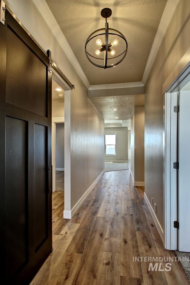 hallway with a barn door, baseboards, hardwood / wood-style flooring, crown molding, and a notable chandelier