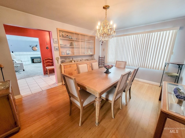 dining area featuring an inviting chandelier, a fireplace, baseboards, and light wood-style floors