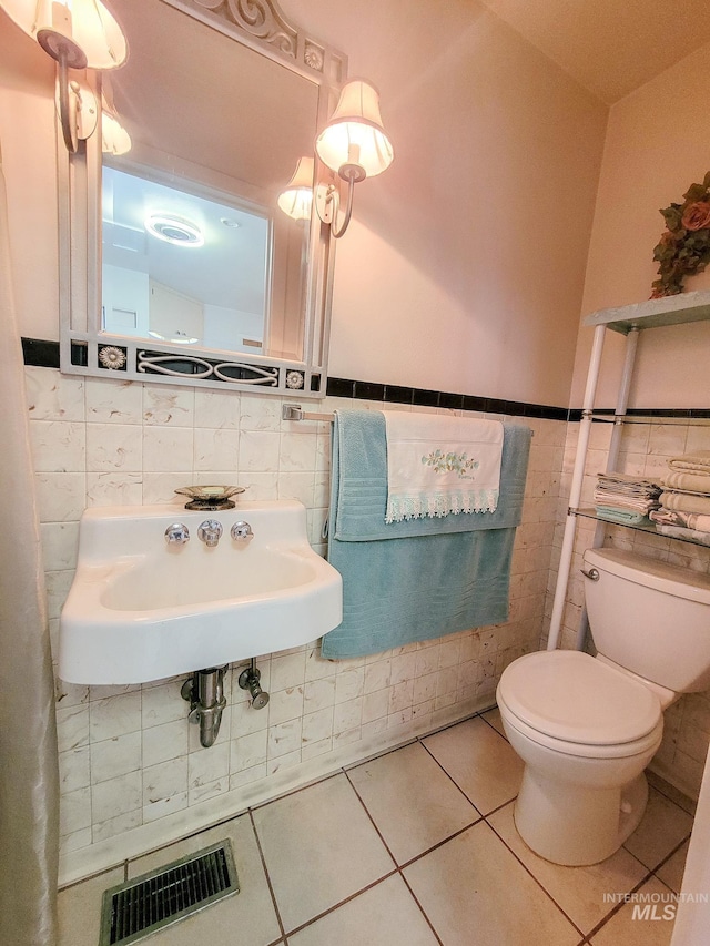 bathroom featuring tile patterned flooring, toilet, a sink, visible vents, and tile walls